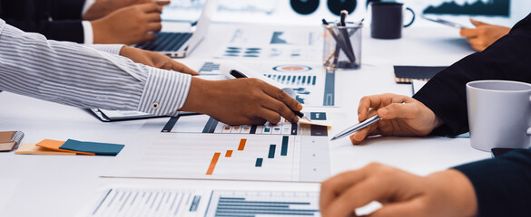 A diverse business team engages in active collaboration at a modern office setting. They analyze charts and graphs while discussing strategies over laptops and documents. SACTR