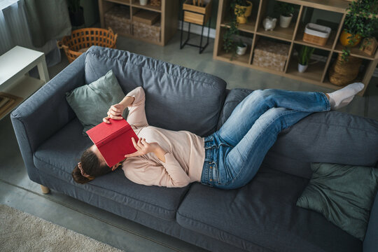 Woman relaxing on sofa with book covering face