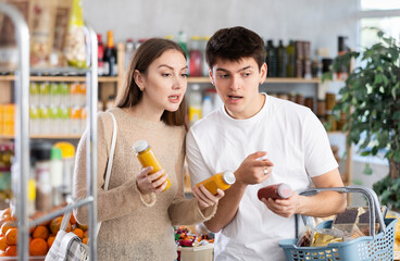 Married young couple in big supermarket buys bottle of smoothie