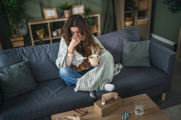 Woman with cold blowing nose holding warm drink at home