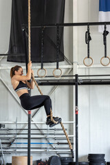 Athletic young woman training rope climbing indoors