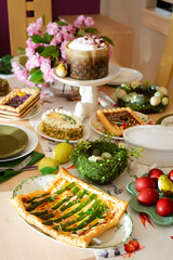 A set and decorated Easter table with festive appetizers, pastries, a baked leg of lamb and painted eggs