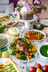 A set and decorated Easter table with festive appetizers, pastries, a baked leg of lamb and painted eggs