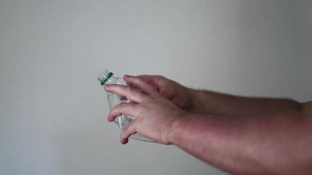 Horizontal 4K video close up. 60 fps. Male hand squeezes, crushes and breaks water bottle. Concept of zero waste, earth day, reuse, storage, eco problem, cleaning plastic pollution, drink, trash