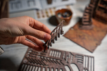 Close-up of a detailed wooden miniature library model with spiral staircase and bookshelves. A human hand carefully assembles the tiny interior, showcasing craftsmanship, creativity, and hobby modelin © Alisa