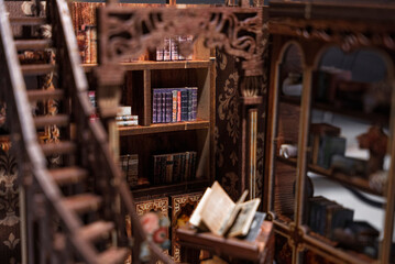 Detailed miniature wooden library interior with spiral staircase, bookshelves and tiny furniture. Close-up of handcrafted dollhouse room showing creativity, hobby, craftsmanship and vintage design. © Alisa