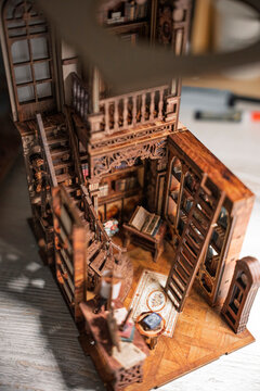 Detailed miniature wooden library interior with spiral staircase, bookshelves and tiny furniture. Close-up of handcrafted dollhouse room showing creativity, hobby, craftsmanship and vintage design.