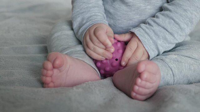 Infant practicing motor skills with colorful toy, Baby exploring tactile textures on soft blanket with ball grasp, Child engaging with sensory objects to develop motor skills and tactile awareness