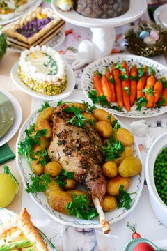 A set and decorated Easter table with festive appetizers, pastries, a baked leg of lamb and painted eggs
