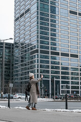 Winter city wanderlust: female tourist walking historic Warsaw old town, pastel facades and holiday lights, cozy coat, scarf and beanie. Urban sightseeing, slow travel, sustainable Europe escape eco.