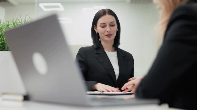 Businesswoman in a black suit takes notes during a meeting with a colleague, showing collaboration and engagement, ending with a handshake and agreement in a modern office. Concept collaboration, busi