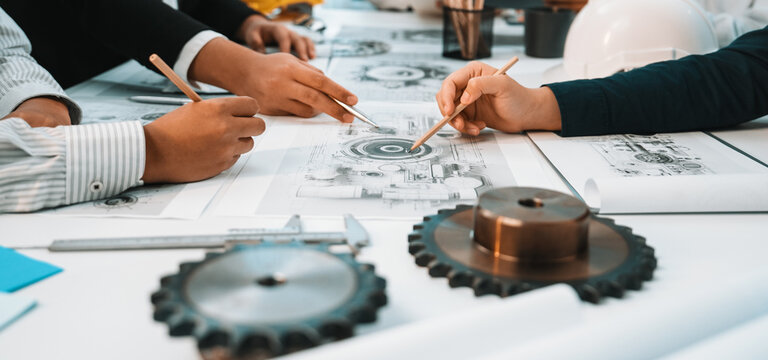Close-up of hands tracing over technical drawings and mechanical designs during an engineering meeting, showcasing collaboration and innovative thinking in a creative workspace. SACTR