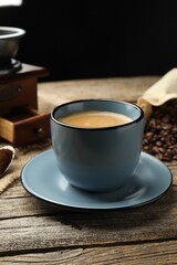 Aromatic coffee in cup and beans on wooden table, closeup