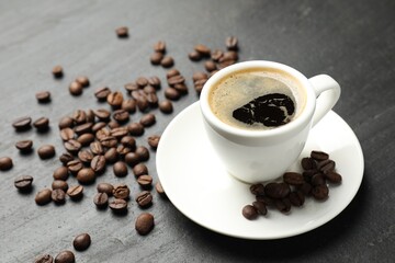Obraz premium Refreshing coffee in cup and beans on dark textured table, closeup