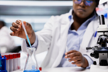 Close up of quality control analyst pipetting agent into blue test tube sample to improve chemical formulation. Research facility expert observing reaction in test tube to verify scientific hypothesis