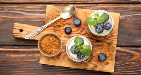 Tasty trifle dessert with whipped cream, mint and berries in glass jars on wooden table, flat lay