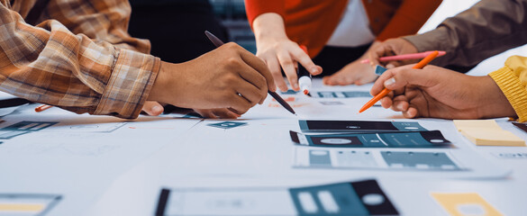 A diverse team gathers around a table filled with colorful sketches and tools, engaged in user interface design. The atmosphere is collaborative and innovative. SACTR