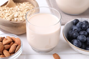 Almond milk, oat flakes, nuts and blueberries on white wooden table, closeup