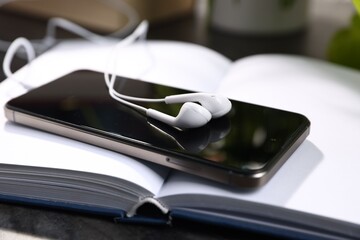 Smartphone with earphones and book on black table, closeup