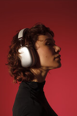 Profile portrait of a woman wearing headphones on red background. Music listening, focus, calm mood, lifestyle and audio concept. © Sergey Chumakov