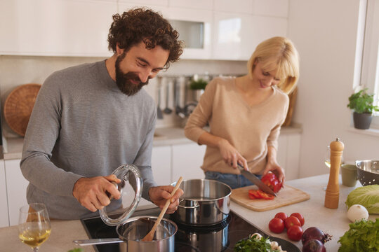 Two people work together in a bright, contemporary kitchen, chopping vegetables and stirring pots to create a delicious meal, enjoying the process of cooking side by side.