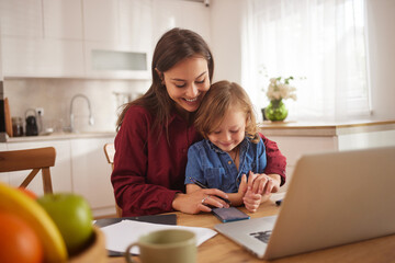 A mother and her young child engage in a fun activity at the kitchen table, fostering connection and creativity together during a relaxed day at home.