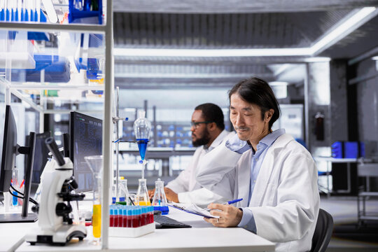 Fatigued laboratory engineer stretching while using computer for DNA data analysis. Tired Asian research facility worker relaxing neck muscles, using bioinformatics genomics software on PC in lab - Powered by Adobe