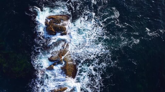 Crystal-clear waters swirl around rocky formations as waves relentlessly pound the coast, showcasing nature's beauty in a tranquil seaside setting at dusk.