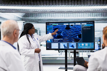 Lab manager briefing research professionals on new experimental protocols. Laboratory team leader using digital display to explain complex biological data to staff members
