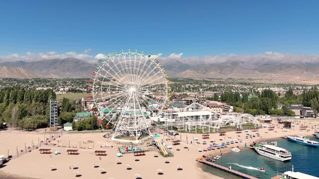 Ferris wheel by Issyk-Kul Lake with scenic mountains in the background, a popular tourist spot.