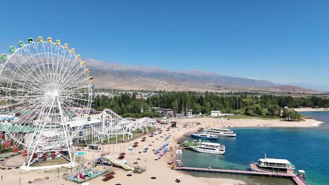 Ferris wheel by Issyk-Kul Lake with scenic mountains in the background, a popular tourist spot.