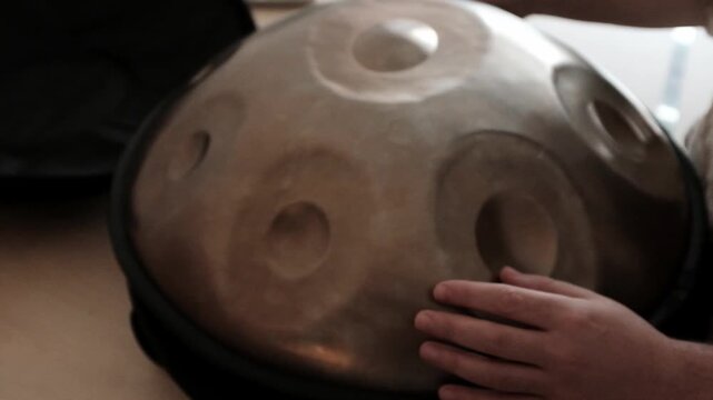 Man is playing hand pan musical instrument. Closeup slow motion video. Hang drum relaxing percussion instrument for meditative sound for slow practices and yoga.