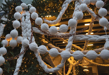 Close-up of festive white rope and braided Christmas decoration with warm fairy lights at winter holiday market