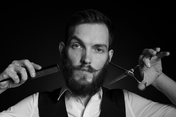 Man with stylish mustache holding barber's tools on dark background. Black and white effect