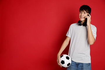 Teenage boy with soccer ball talking on smartphone against red background, space for text