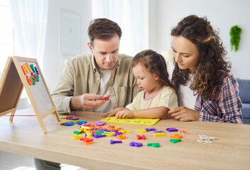 Fototapeta premium Family parents teaching daughter alphabet at home. They guide the child with colorful letters, encouraging early learning, motor skills, and playful education. Family learning at home concept.