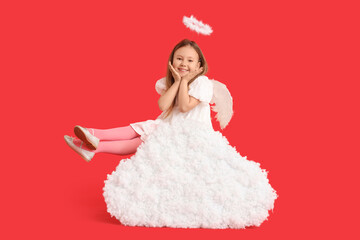 Fototapeta premium Cute little girl dressed as cupid sitting on cloud against red background. Valentine's Day celebration