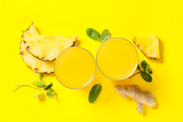 Glasses of fresh pineapple juice with mint and ginger root on yellow background