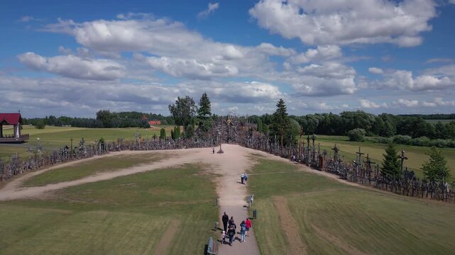 Hillside covered in countless crosses, with people walking on paths beneath a cloudy blue sky.