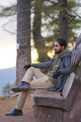Fototapeta premium Man sitting on a wooden bench in a forest at sunset. Ideal for travel, relaxation, and outdoor lifestyle concepts.