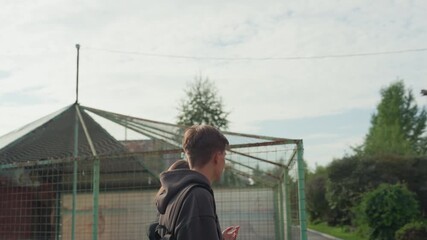 white teenage friends chatting by fence, playful smiles and candid glances, casual hoodies and backpacks, sunlit clouds and suburban greenery, easygoing banter and youthful chemistry, close framing