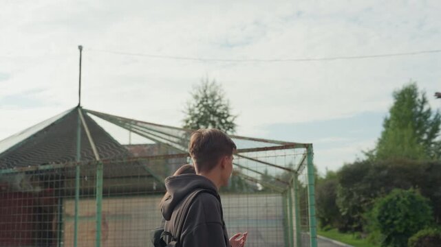 white teenage friends chatting by fence, playful smiles and candid glances, casual hoodies and backpacks, sunlit clouds and suburban greenery, easygoing banter and youthful chemistry, close framing