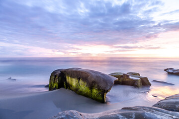 Long exposure photography of the tide wrapping around moss covered rocks at sunset on a La Jolla Beach