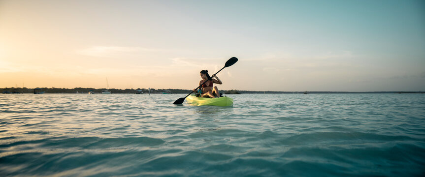 Hermosa mujer joven latina en bikini, navegando en kayak en el mar, al atardecer