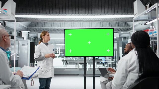 Green screen display used by biochemist presenting innovative drug development findings to team in laboratory. Molecular biologist pointing at mockup screen during briefing training meeting, camera A