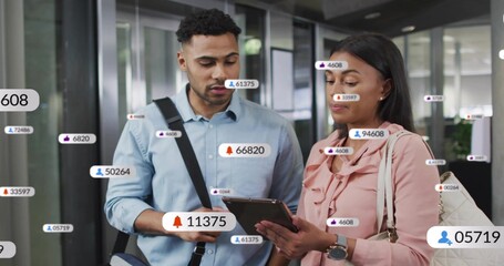 Discussing coworkers in blue shirt and pink blouse checking tablet in office, with notifications