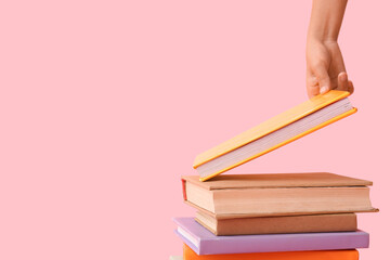 Child's hand with stack of books on pink background