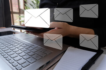 Business person holding a cell phone while working on his computer and there are several email icons around