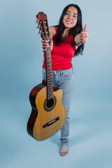 Fototapeta premium portrait of young latin teenager girl playing guitar with copy space on blue background in Mexico Latin America, Hispanic woman holding a musical instrument 