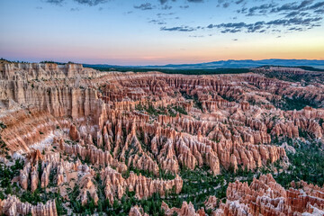 A beautiful landscape of red rock formations with a sunset in the background. The sky is filled with clouds, creating a serene and peaceful atmosphere